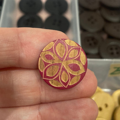 Hand holding a decorative button with a collection of buttons in the background.