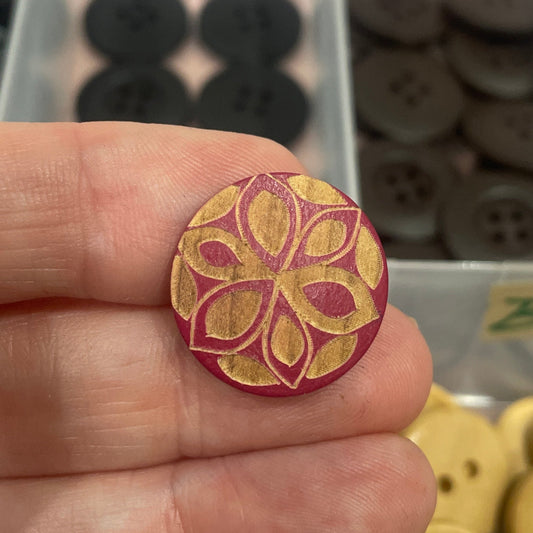 Hand holding a decorative button with a collection of buttons in the background.