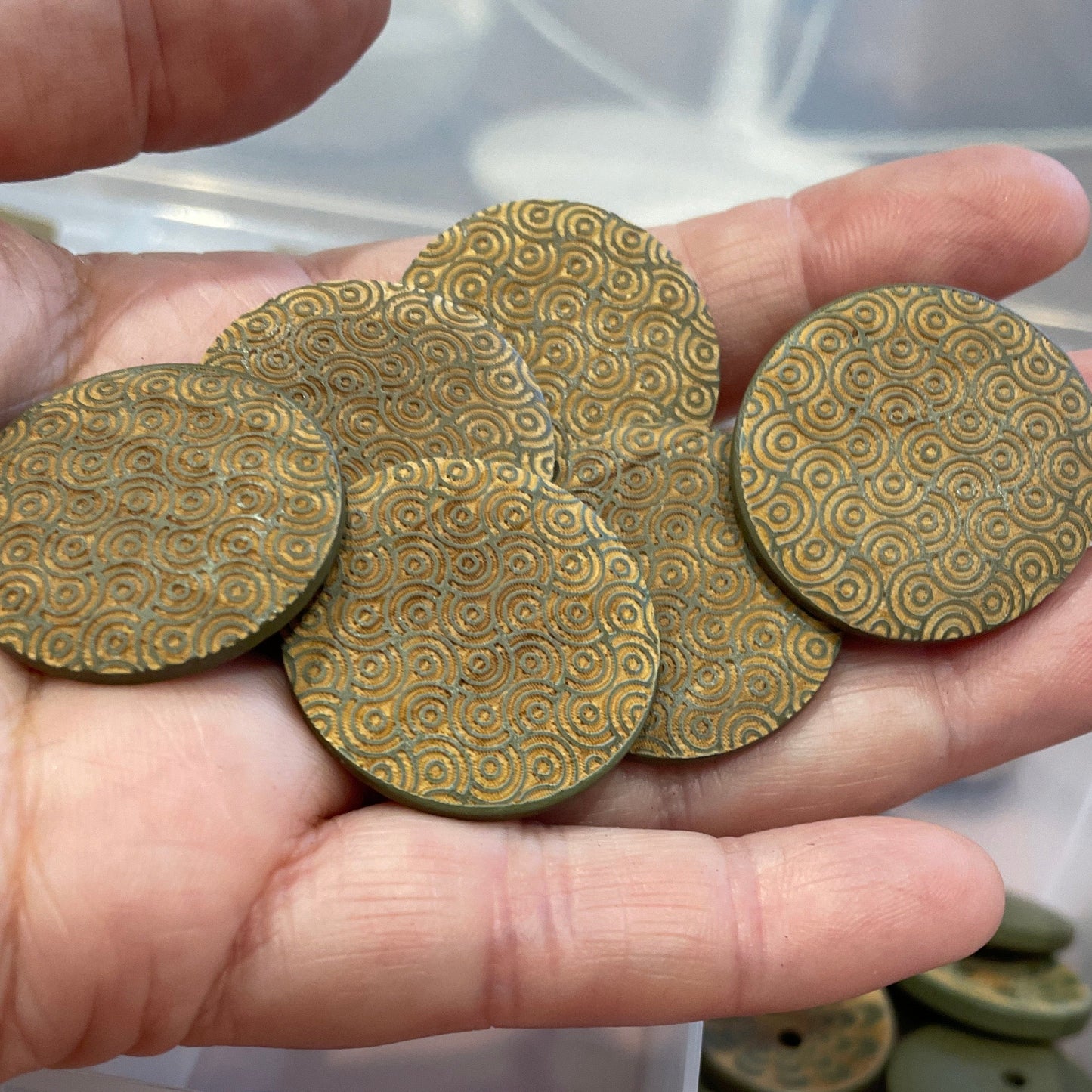 Hand holding decorative buttons with a container of similar buttons  in the background.