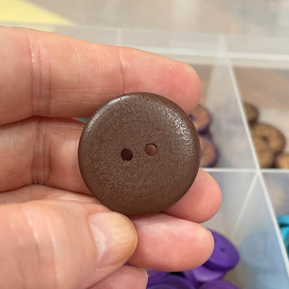 Brown button held in hand with container of buttons in the background