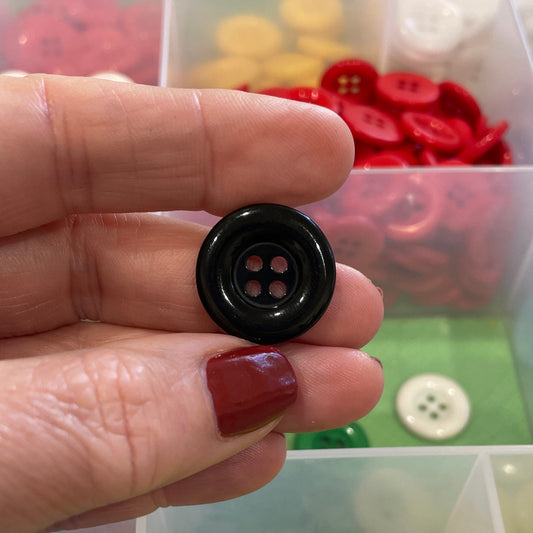 Hand holding a black button with a display of colorful buttons in the background