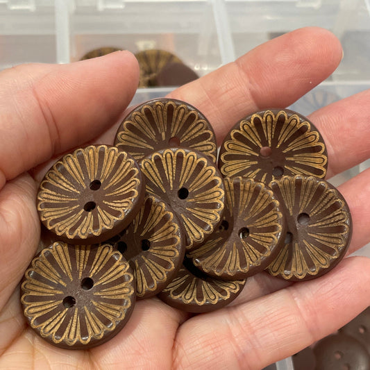 Hand holding bronze buttons with a container of various buttons in the background