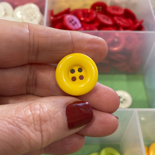 Hand holding a yellow button with a colorful button collection in the background