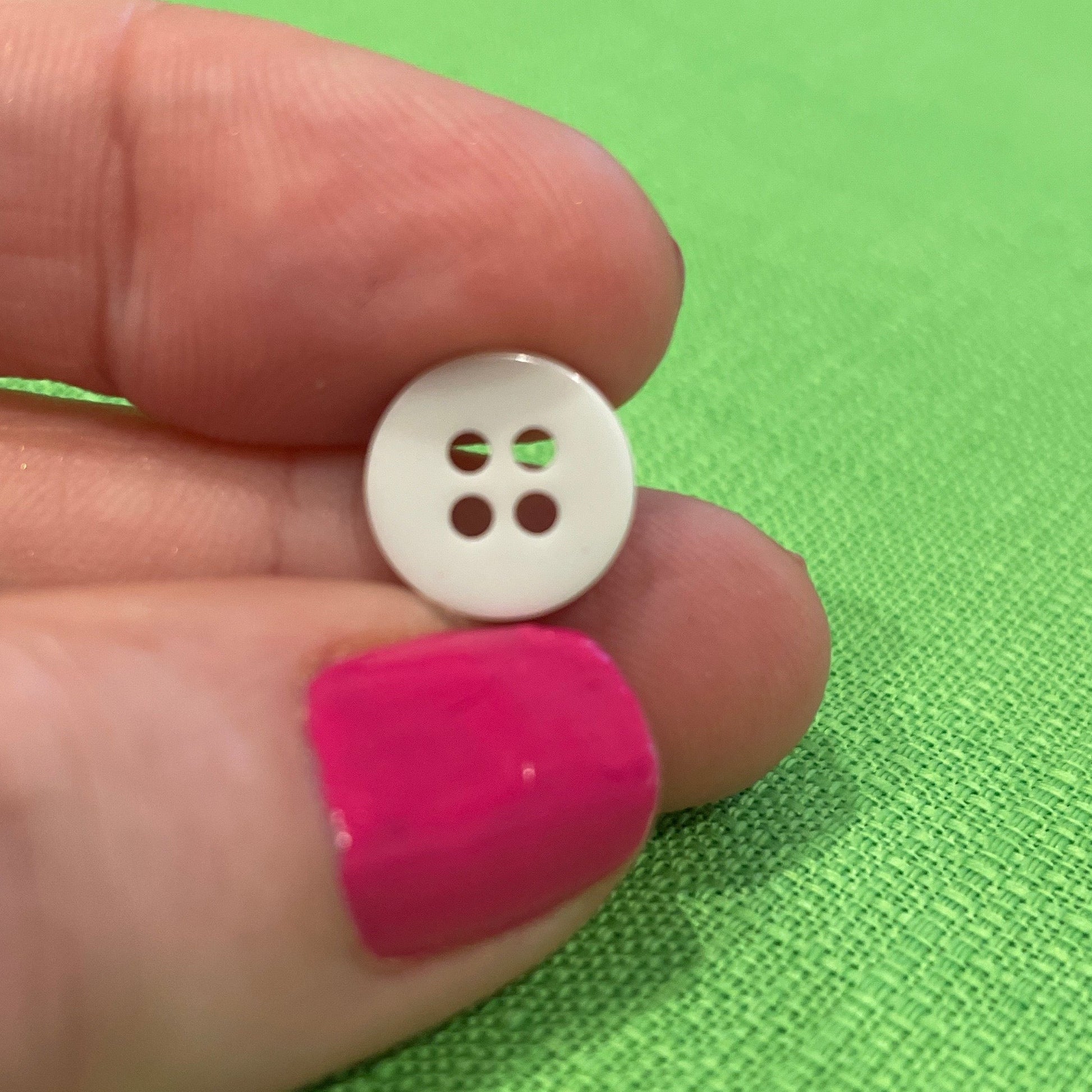 White button held between fingers against a green background