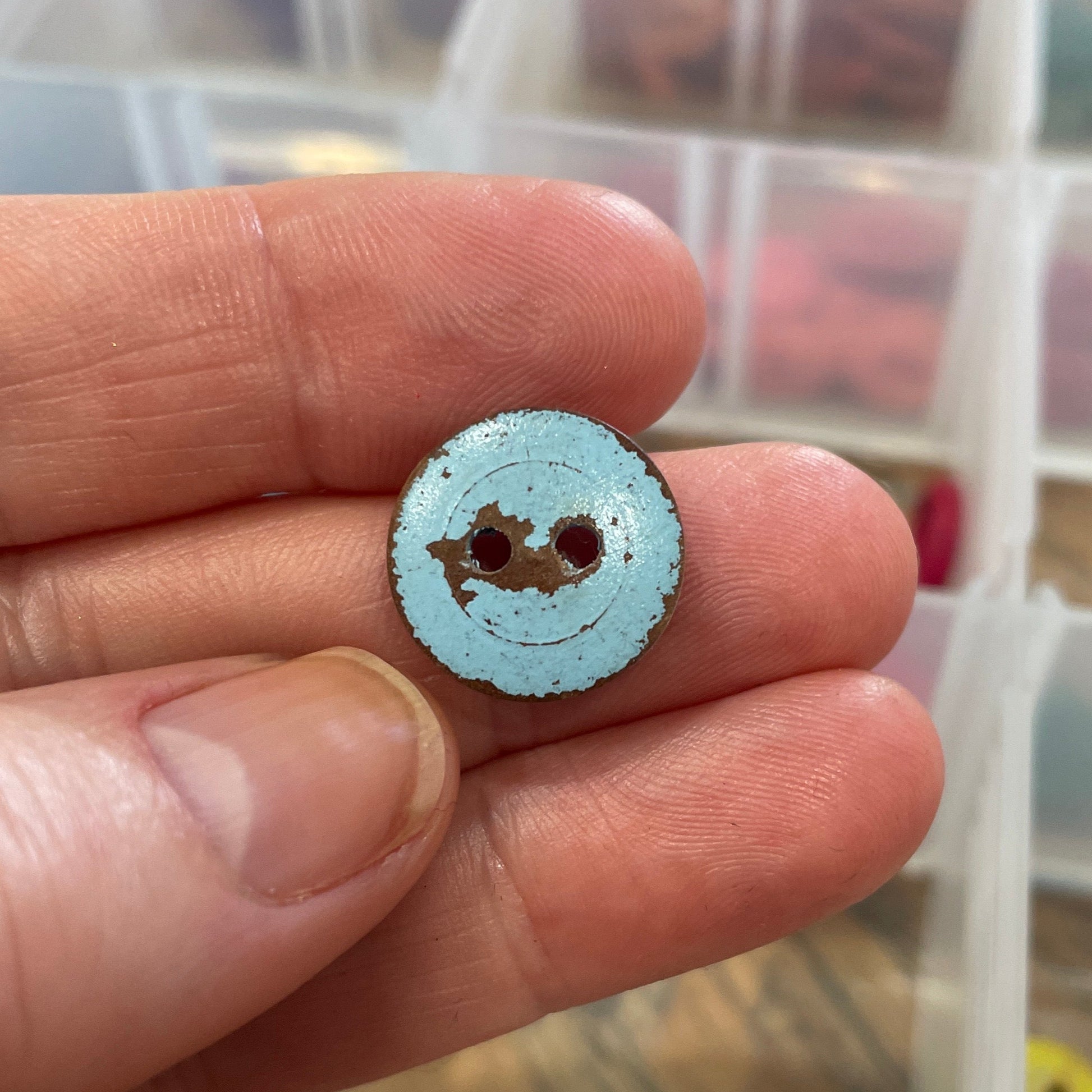 Small round button held between fingers with a container of buttons in the background
