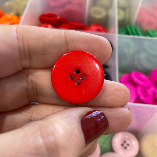 Hand holding a red button with a background of various buttons in a box