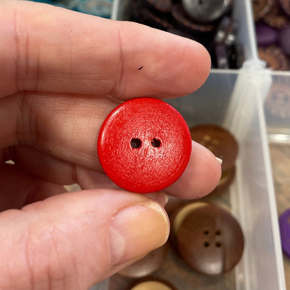 Hand holding a red button with a container of various buttons in the background
