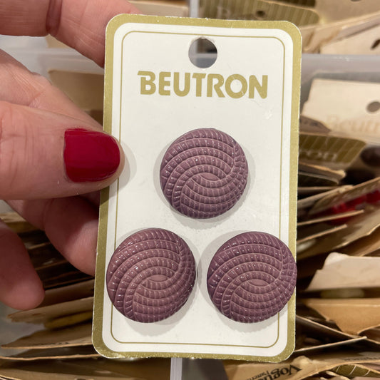 Purple circular buttons on a Beutron card held by a hand with red nail polish.