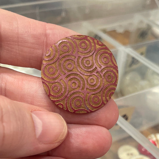 Hand holding a decorative button with a container of buttons in the background