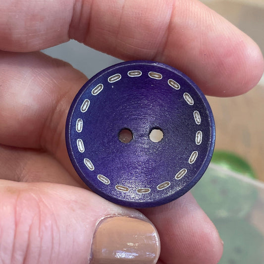 Hand holding a purple button with white dots, blurred background of buttons