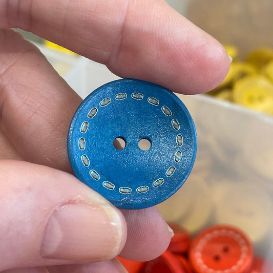 Hand holding a blue button with a container of orange buttons in the background