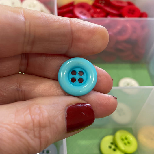 Hand holding a blue button with a container of colorful buttons in the background