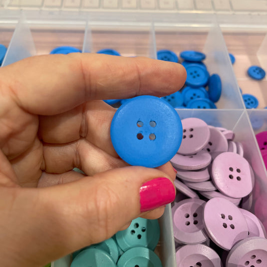 Hand holding a blue button with a container of colorful buttons in the background