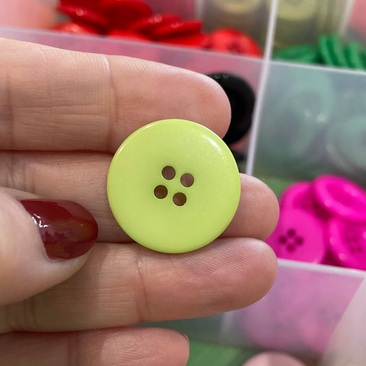 Hand holding a yellow button with a colorful button collection in the background