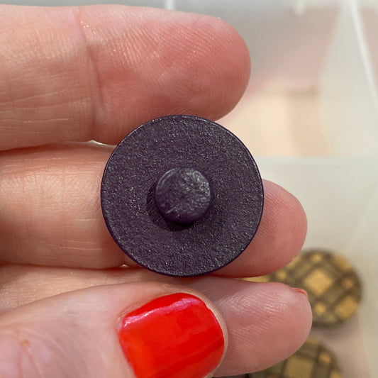 Hand holding a round black object with buttons in the background