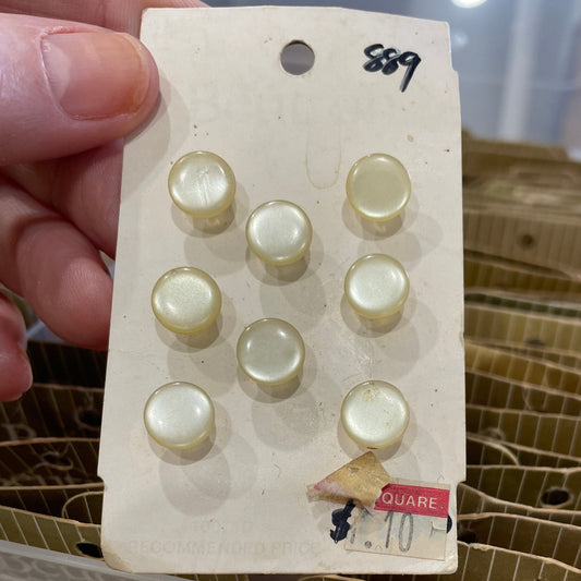 Card with round buttons held by a hand, with a clear container filled with similar items in the background.