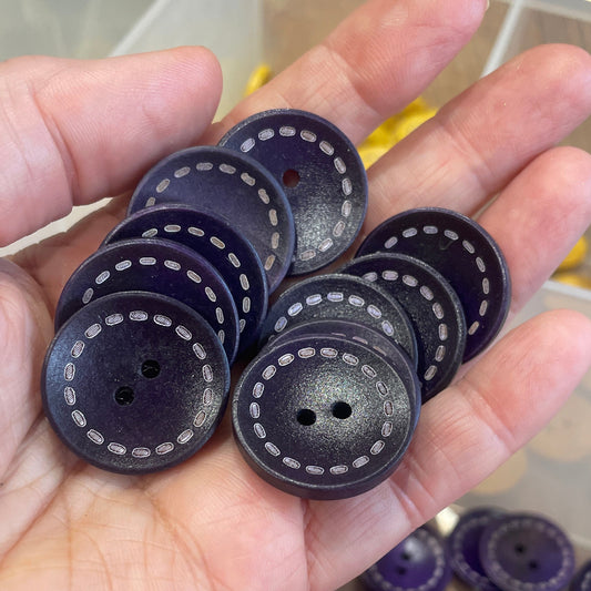 Hand holding purple buttons with a container of buttons in the background