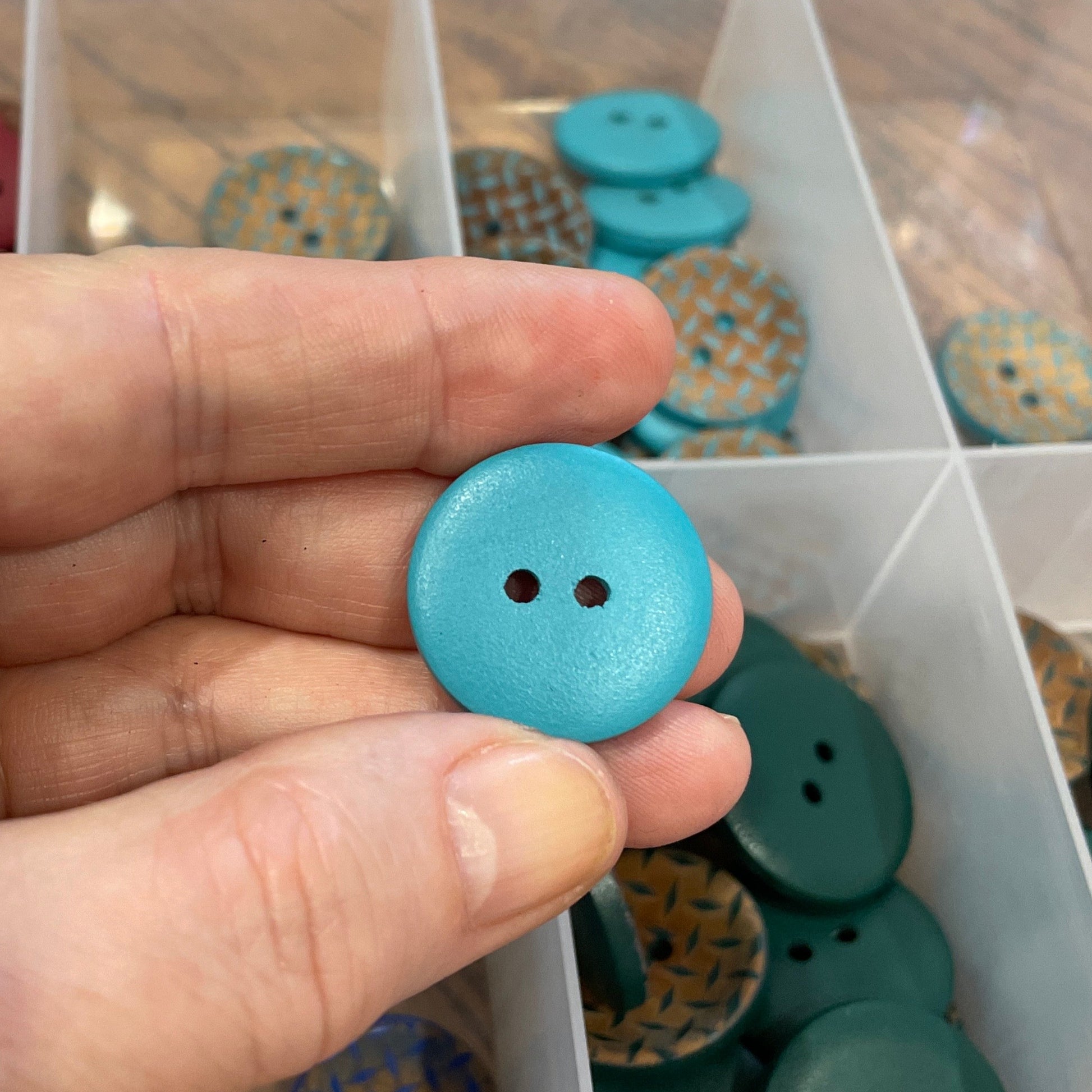 Hand holding a blue button with a container of assorted buttons in the background