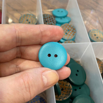 Hand holding a blue button with a container of assorted buttons in the background