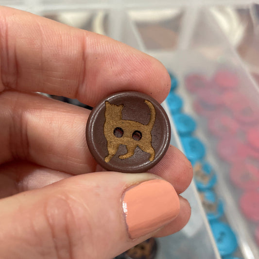 Hand holding a brown button against a background of a button collection in a box.