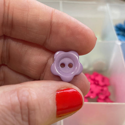 Hand holding a purple flower-shaped button with a colorful background of buttons