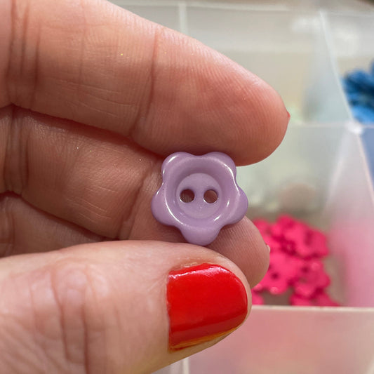 Hand holding a purple flower-shaped button with a colorful background of buttons