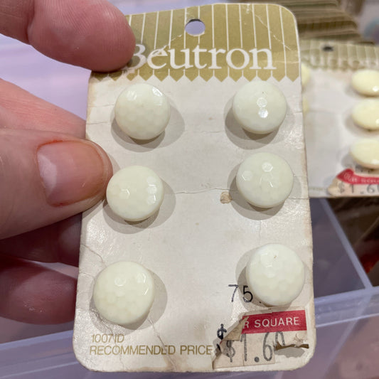 Hand holding a small pack of white buttons with 'Becton' branding.