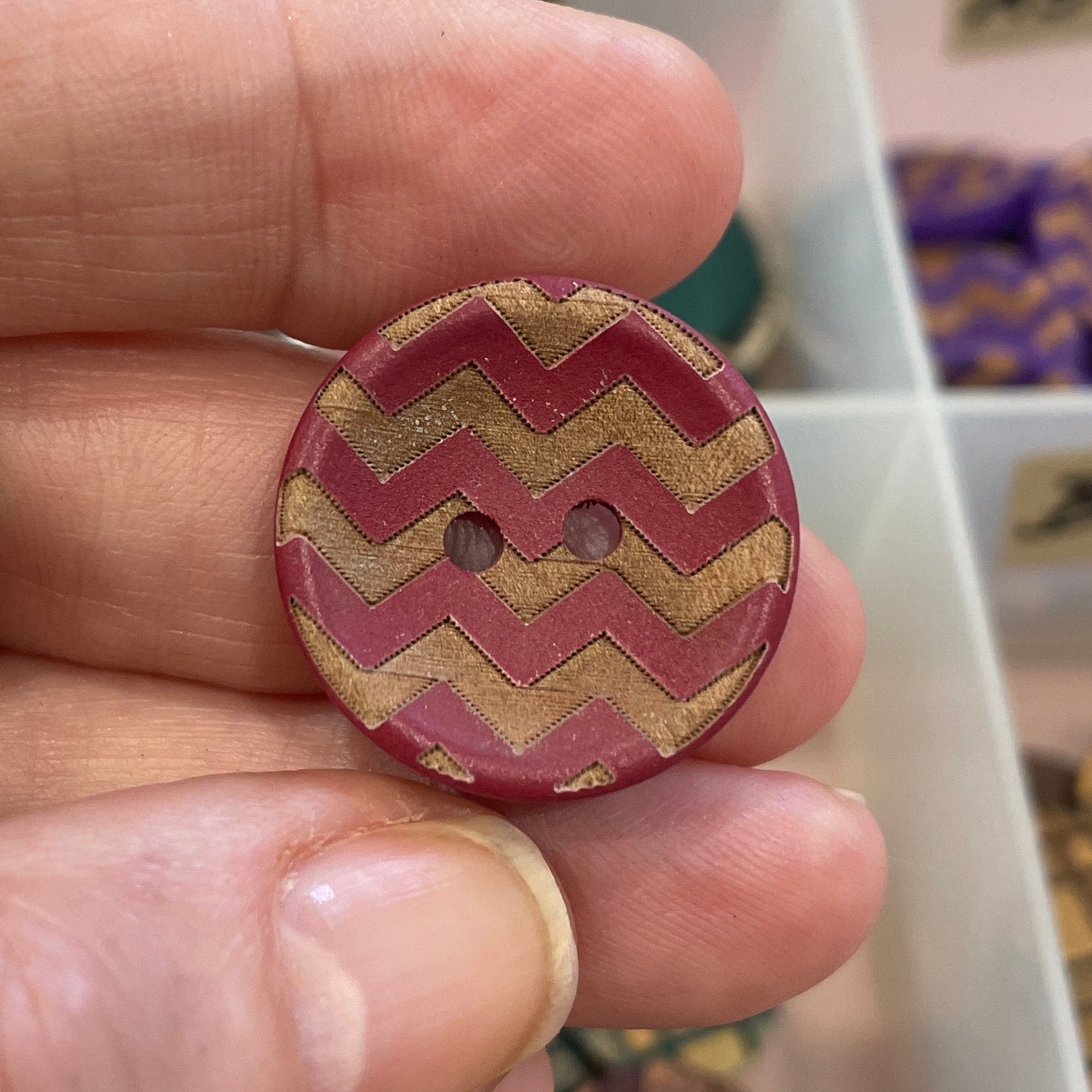 Hand holding a zigzag patterned button with a background of a button organizer.