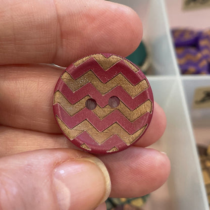 Hand holding a zigzag patterned button with a background of a button organizer.