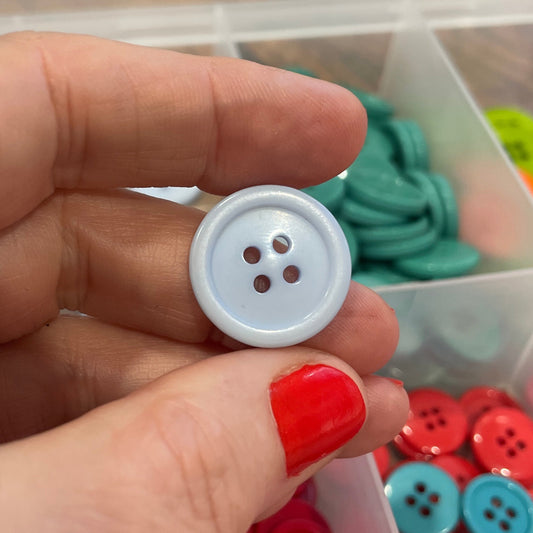 Hand holding a white button with containers of colorful buttons in the background