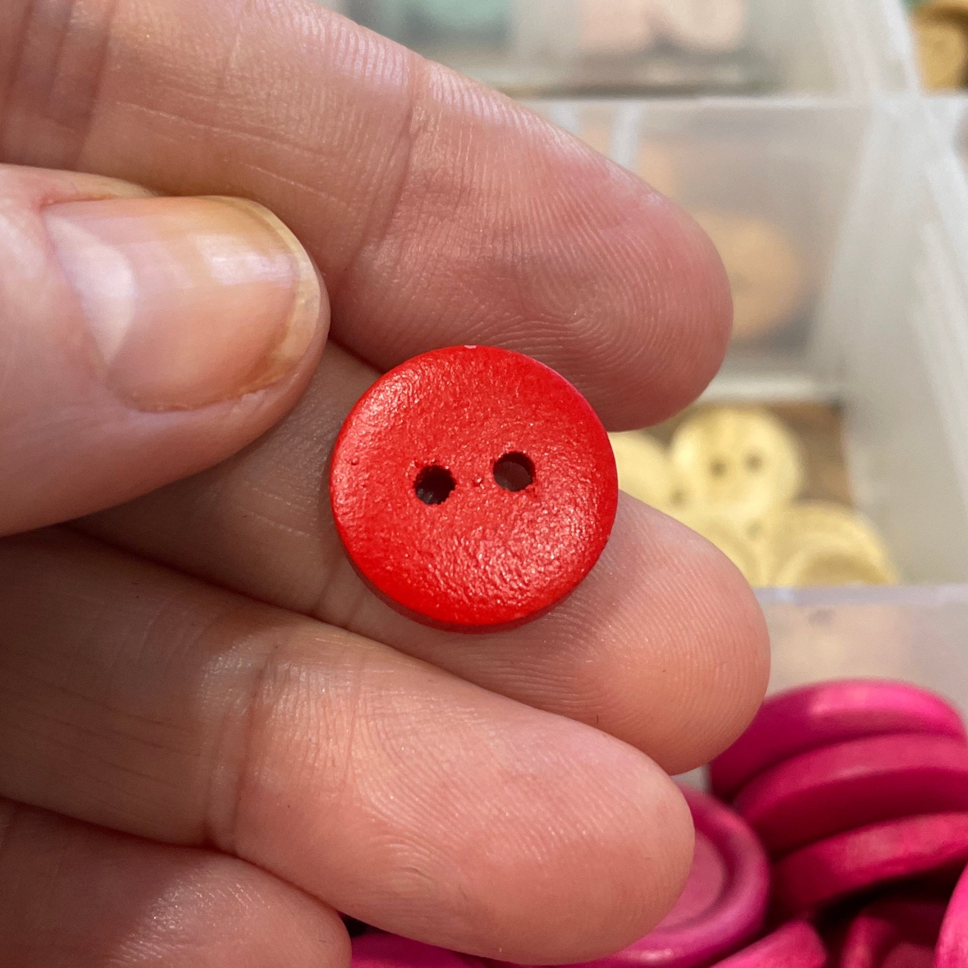 Red button held between fingers with pink and yellow buttons in the background