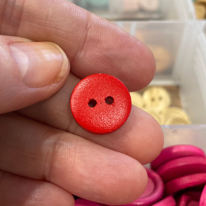 Red button held between fingers with pink and yellow buttons in the background