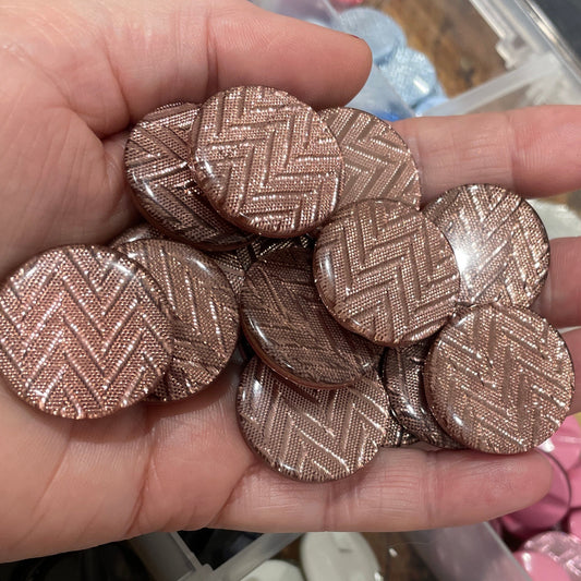 Hand holding metallic buttons with a container of various colored buttons in the background