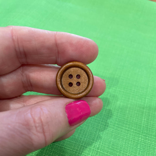 Brown button held between fingers against a green fabric background