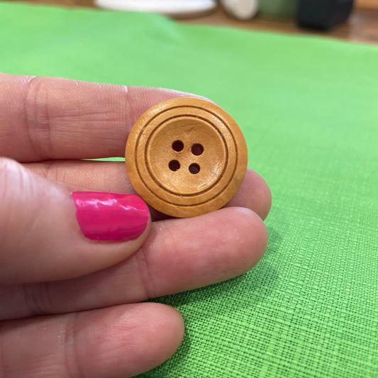 Wooden button held between fingers against a green fabric background