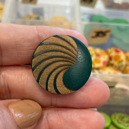 Hand holding a decorative button with a swirling pattern, blurred background of button collection.
