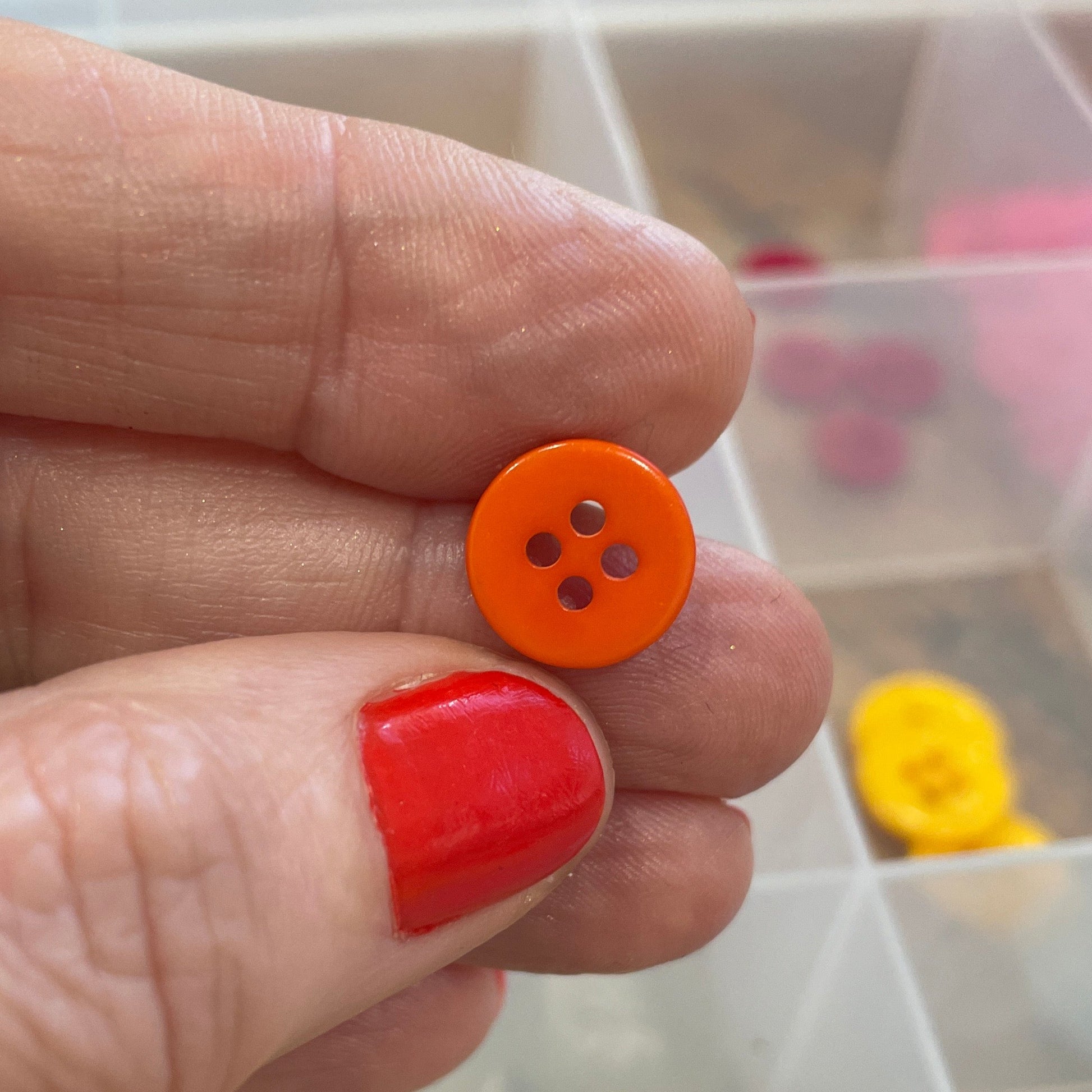 Hand holding an orange button with a clear container of buttons in the background