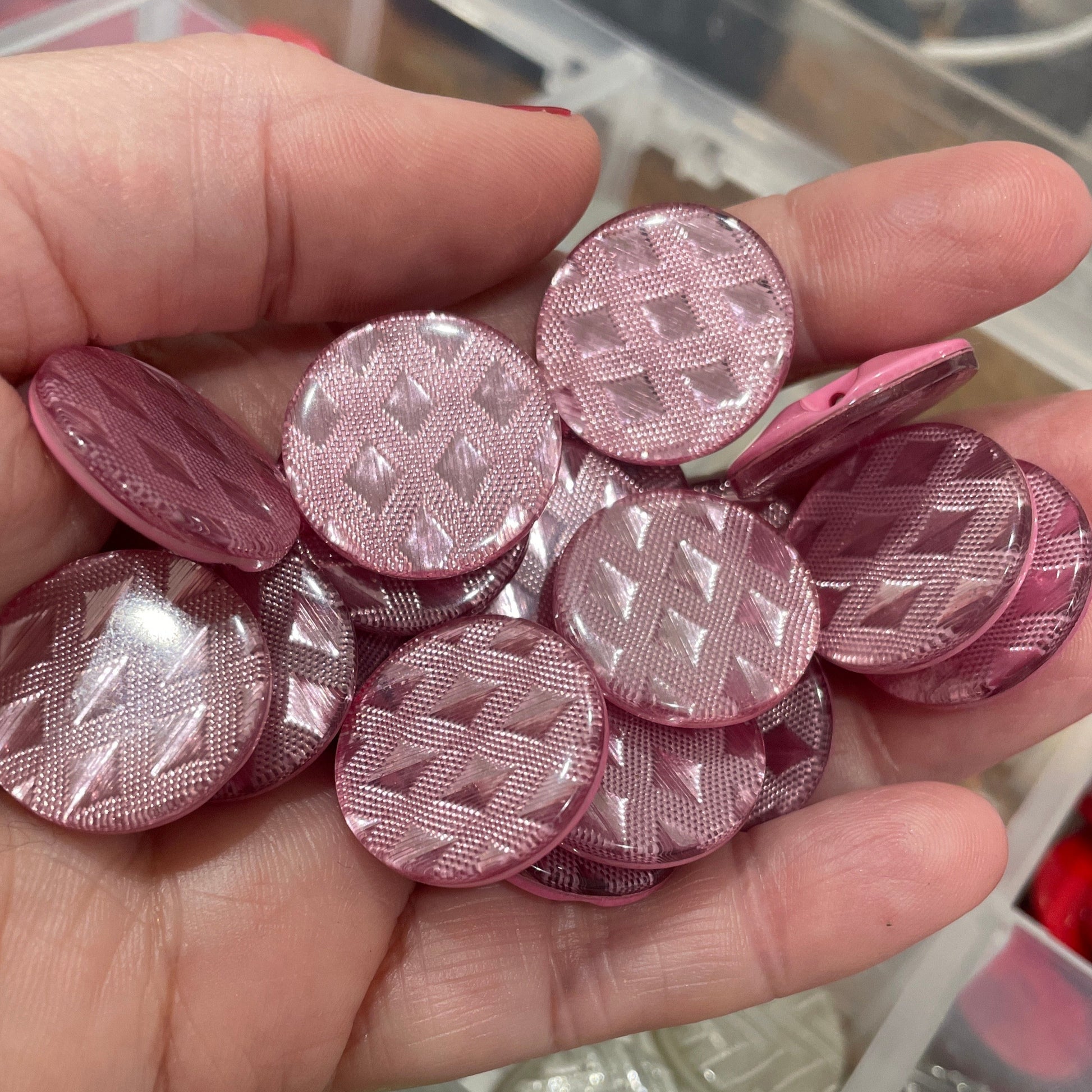 Hand holding pink textured buttons with a container of various buttons in the background