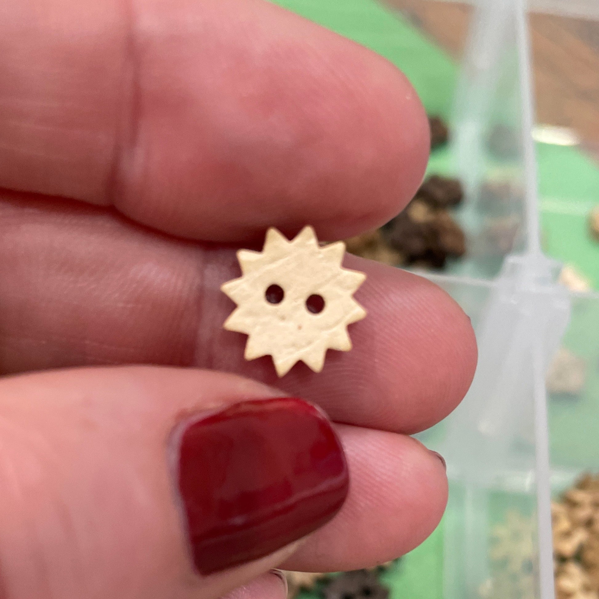 Hand holding a small wooden button  with a collection of buttons in the background.