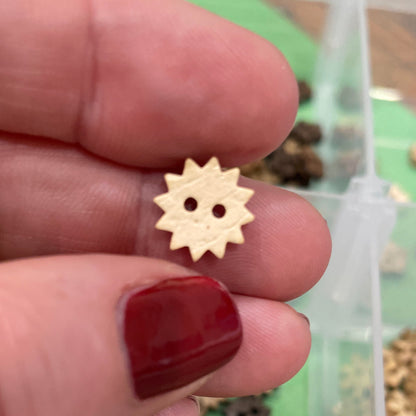 Hand holding a small wooden button  with a collection of buttons in the background.