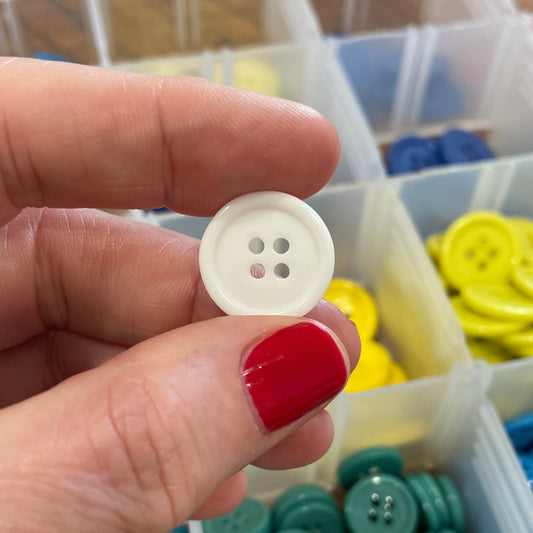 Hand holding a white button with a container of colorful buttons in the background