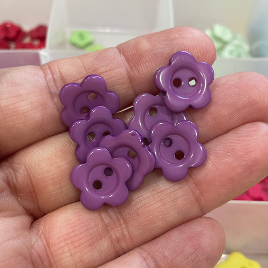 Hand holding purple flower-shaped buttons with a colorful background of similar buttons.