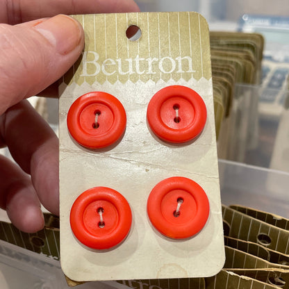 Hand holding a package of red buttons with a brand label.