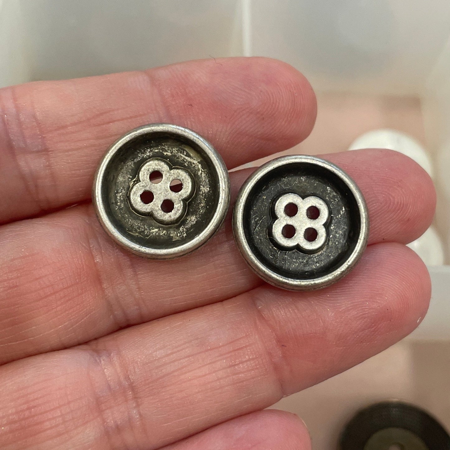 Three metal buttons held in a hand with a grid of buttons in the background