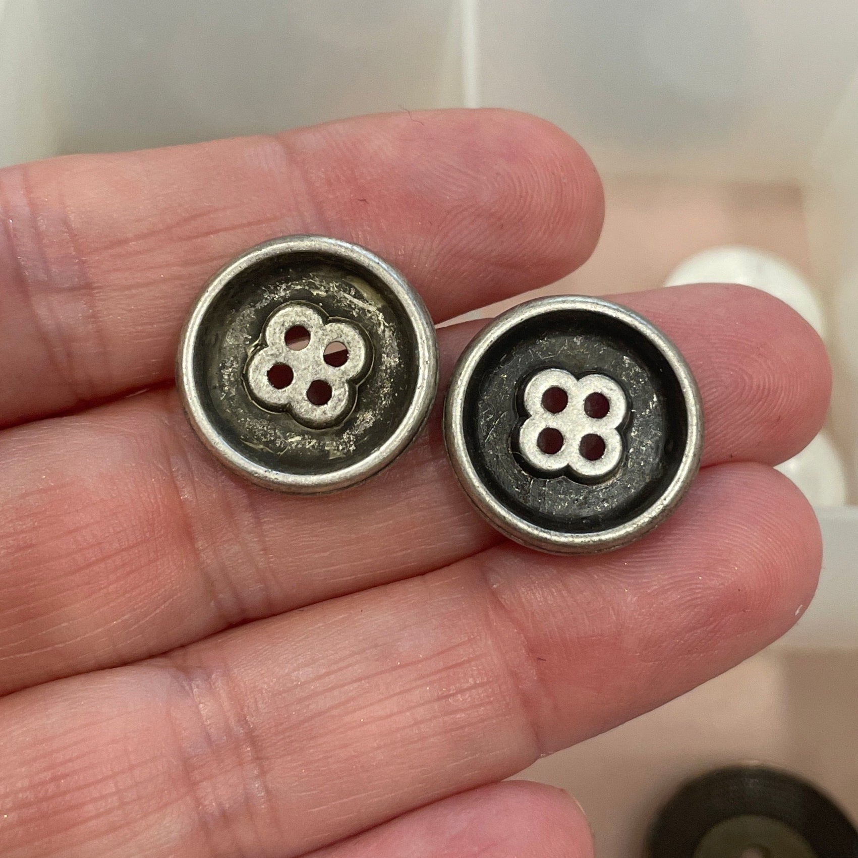 Three metal buttons held in a hand with a grid of buttons in the background