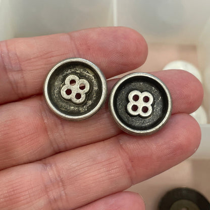 Three metal buttons held in a hand with a grid of buttons in the background