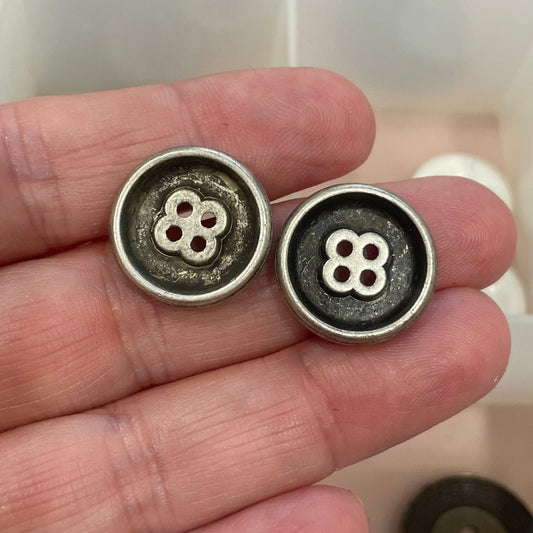 Three metal buttons held in a hand with a grid of buttons in the background
