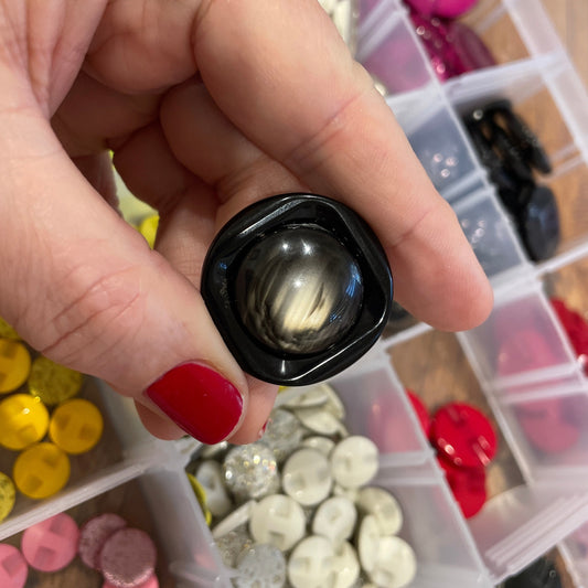 Hand holding a black button with a collection of buttons in the background