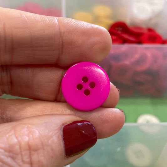 Hand holding a pink button with a background of colorful buttons in a organizer.