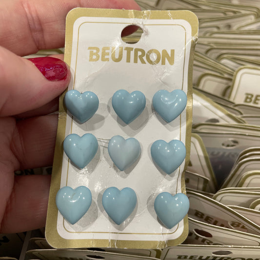 Packaged blue heart-shaped buttons held by a hand with red nail polish.